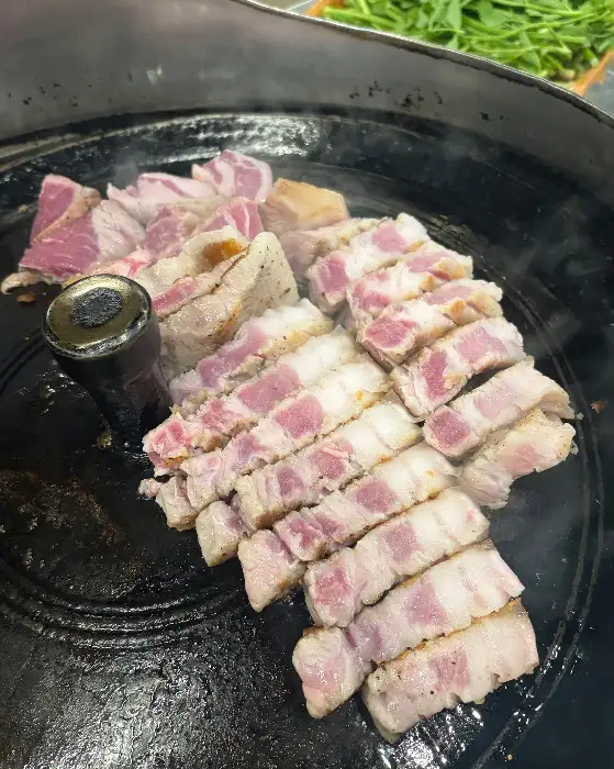 솥뚜껑 위에서 바삭하게 익어가는 삼겹살 조각들