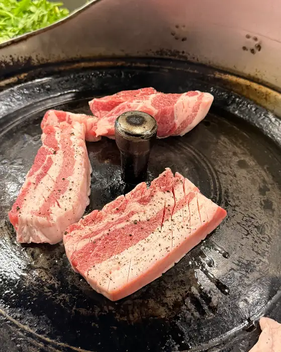 큼직한 삼겹살 덩어리가 솥뚜껑 위에 올려져 익고 있습니다.