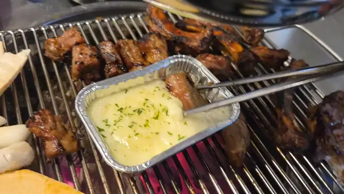 집게로 쪽갈비를 치즈 소스에 찍는 모습