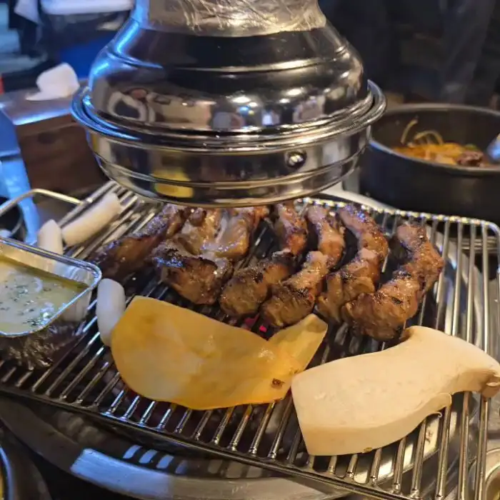 테이블 위 숯불 위에서 구워지는 쪽갈비와 곁들임 메뉴