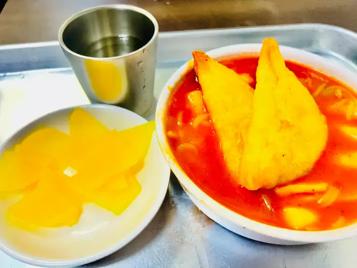 떡볶이, 단무지, 그리고 물이 담긴 컵이 함께 나온 모습