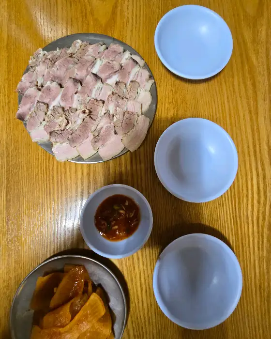 식탁 위에 차려진 푸짐한 음식들. 편육, 동그랑땡, 무김치, 그리고 빈 그릇들이 보입니다.