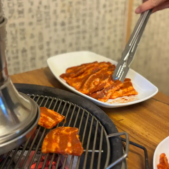 숯불 위에서 구워지고 있는 목살 조각과 집게로 고기를 집는 모습