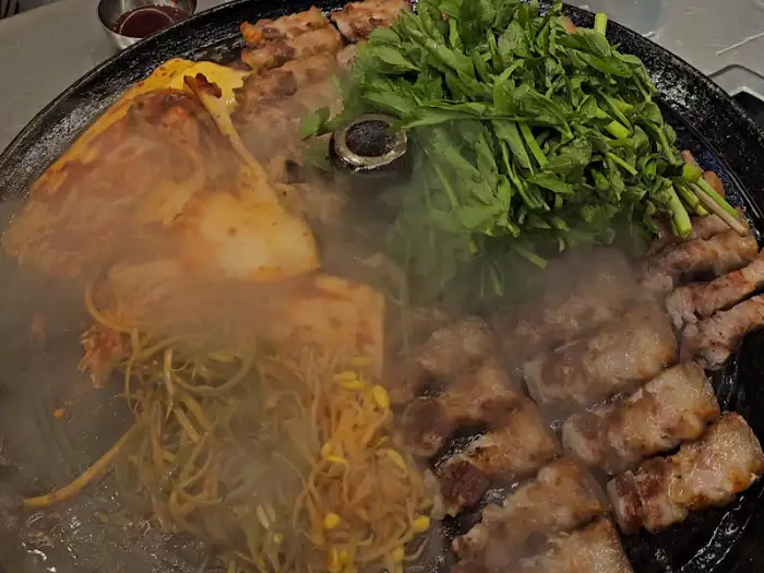불판 위에 고기, 미나리, 콩나물이 함께 익어가는 모습