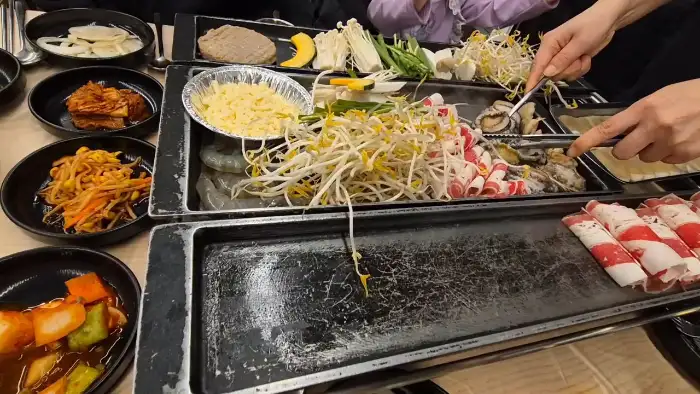 테이블에 놓인 삼합 재료를 직원이 집게로 집어 굽는 모습