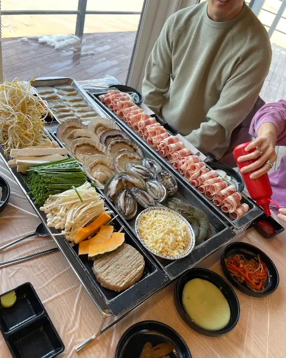 테이블에 놓인 삼합 구성과 손으로 붉은색 소스통을 든 모습