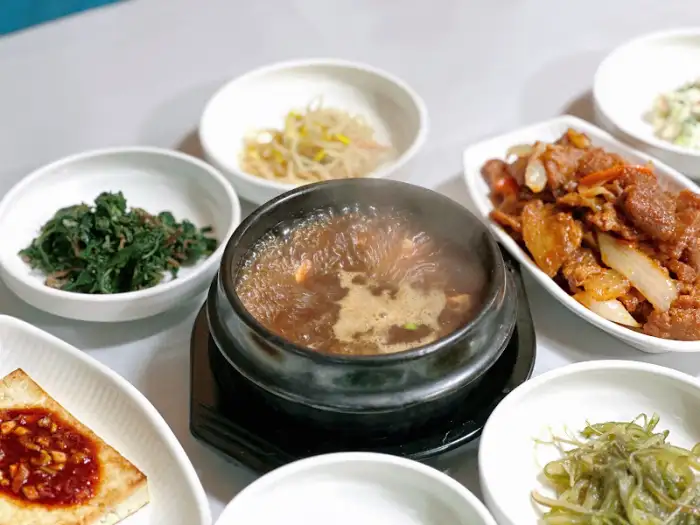 따뜻한 국물이 담긴 뚝배기 요리와 신선한 녹색 채소가 담긴 반찬.