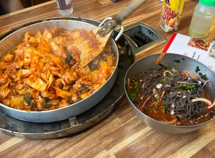 큰 팬에 담긴 닭갈비와 옆에 놓인 비빔 막국수