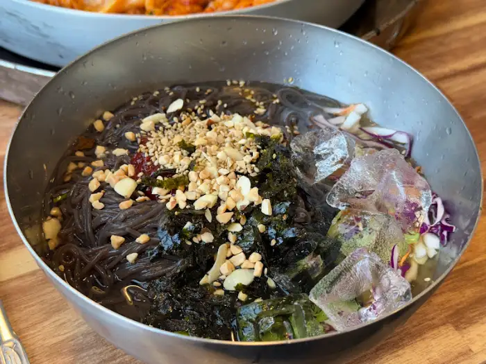 차가운 육수에 말아진 비빔 막국수, 김과 깨가 고명으로 올라가 있다