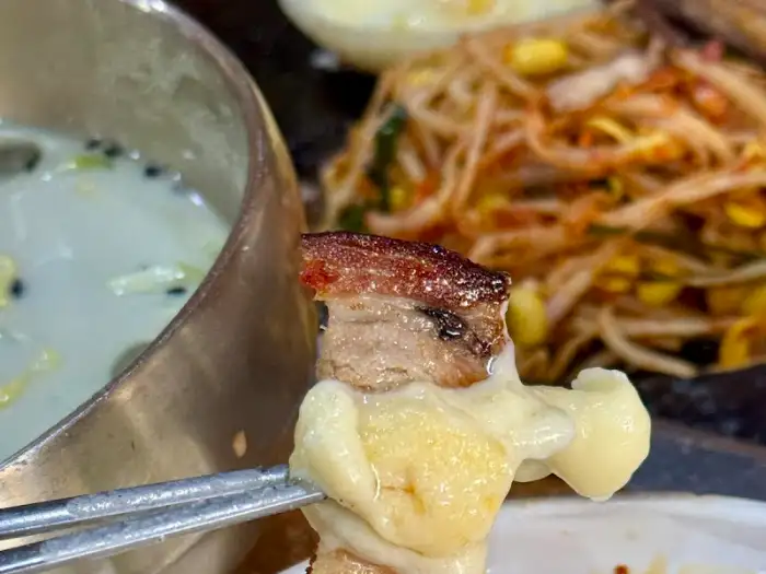 치즈 범벅된 고기 한 점을 집게로 들어 올린 모습