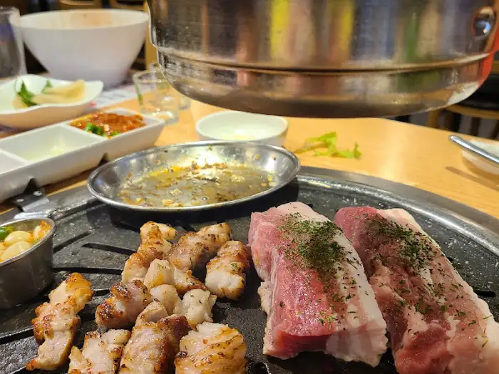 숯불 위에 구워지고 있는 삼겹살과 곁들임 음식