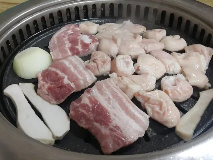 돌판 위에 삼겹살, 버섯, 양파, 막창이 올라가 익고 있는 모습