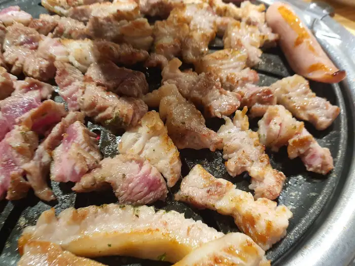 불판 위에서 익어가는 삼겹살과 소시지