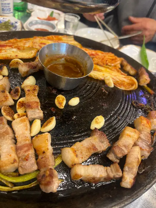 솥뚜껑 위에서 익어가는 삼겹살과 콩나물, 김치