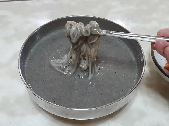 젓가락으로 집어 올린 검은 콩국수 면