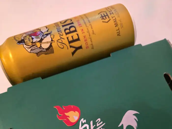 맥주 캔과 닭강정 박스 뚜껑의 일부가 보이는 사진