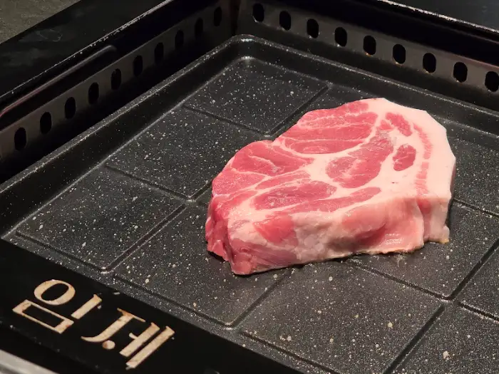 달궈진 불판 위에 신선한 돼지고기 목살이 놓여 있다.
