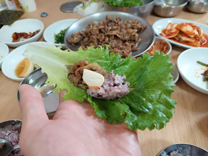 상추 위에 불고기, 밥, 마늘을 올려 싸 먹는 모습. 푸짐하고 맛있어 보입니다.