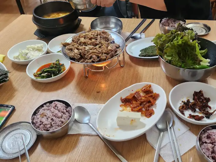 테이블 가득 차려진 밥상 모습. 불고기, 밥, 쌈 채소, 그리고 다양한 밑반찬들이 조화롭게 놓여 있습니다.