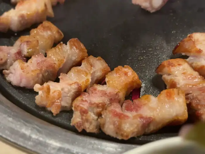 잘 구워진 삼겹살 조각들이 불판 위에 줄지어 놓여 있습니다.