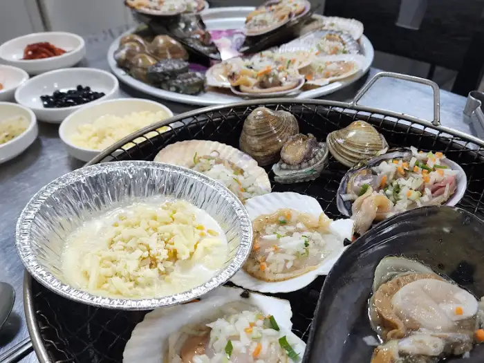 숯불 위에서 구워지고 있는 조개와 곁들임 음식