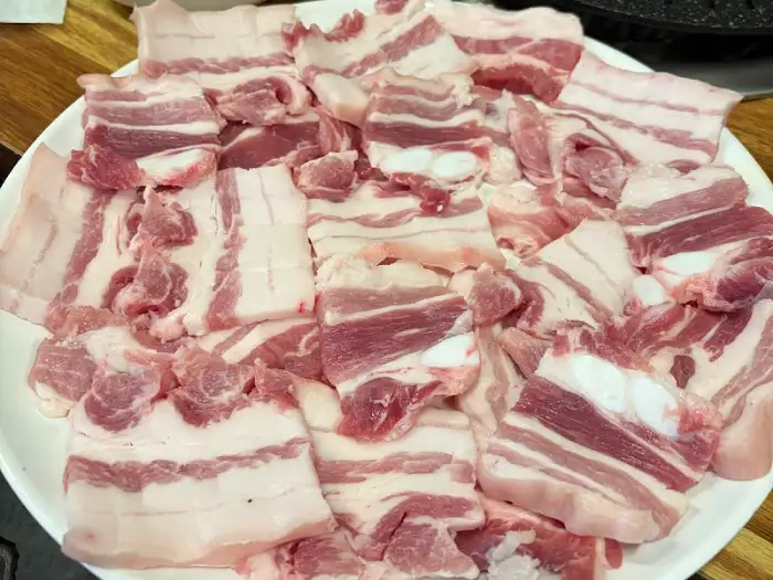기름과 살코기가 적절히 섞인 삼겹살 여러 조각이 접시에 담겨 있습니다.