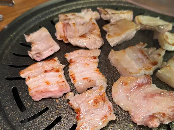 잘 익어가는 삼겹살 조각들이 불판 위에서 노릇하게 구워지고 있습니다.
