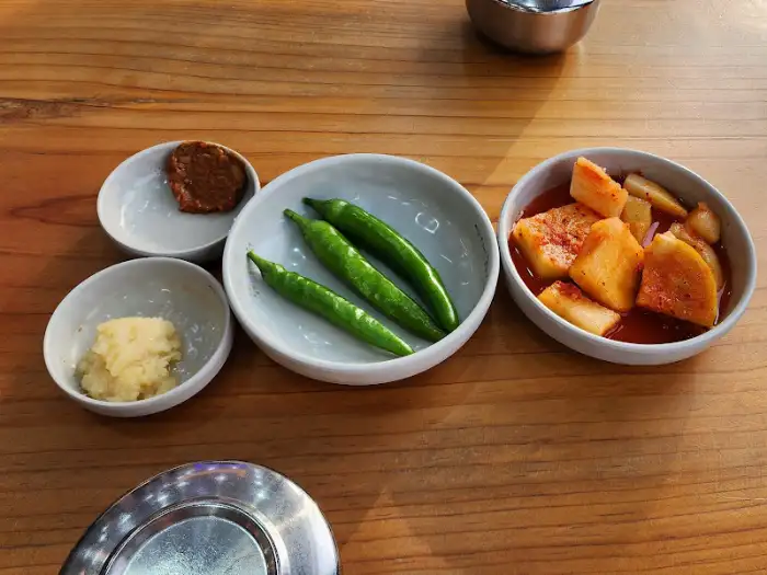 테이블 위에 놓인 밑반찬들: 깍두기, 고추, 쌈장, 다진 마늘