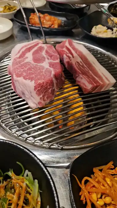 두툼한 흑돼지 목살과 삼겹살이 숯불 위에서 구워지고 있다.