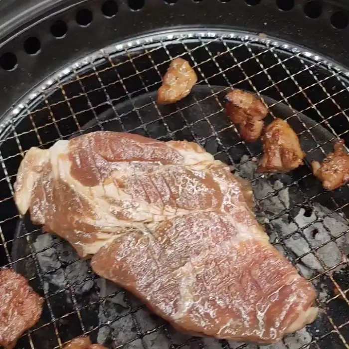 두툼한 고기 덩어리가 불판 위에서 익고 있는 모습