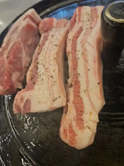 직원이 솥뚜껑 위에서 삼겹살을 정성스럽게 구워주고 있는 모습