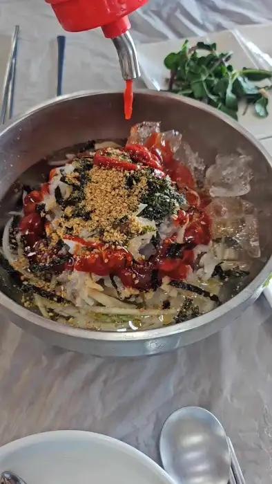 얼음이 동동 띄워진 시원한 물회 위에 양념장과 김가루, 깨소금이 뿌려져 있습니다. 신선한 해산물과 채소가 어우러져 군침을 돌게 합니다.