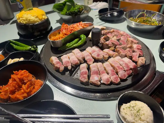 솥뚜껑 주위에 둘러앉은 다양한 밑반찬과 고기