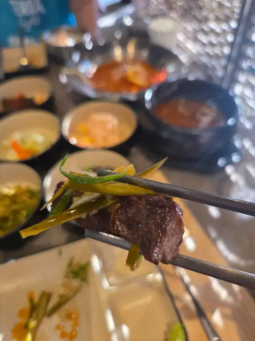 잘 구워진 소고기 한 점을 젓가락으로 집어 파와 함께 먹는 모습