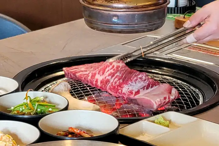 전문 셰프가 집게로 소고기 덩어리를 집어 숯불 위로 옮기는 모습