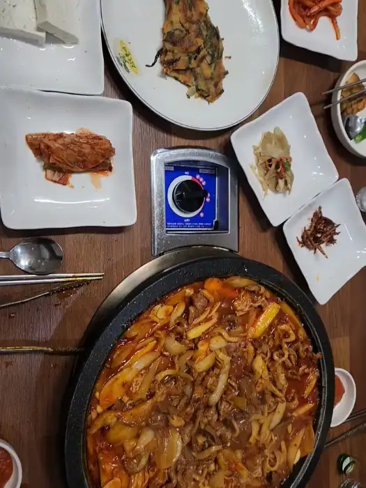 철판 위에서 지글지글 끓고 있는 오리주물럭. 양파, 파, 떡 등이 함께 들어있어 먹음직스럽습니다.