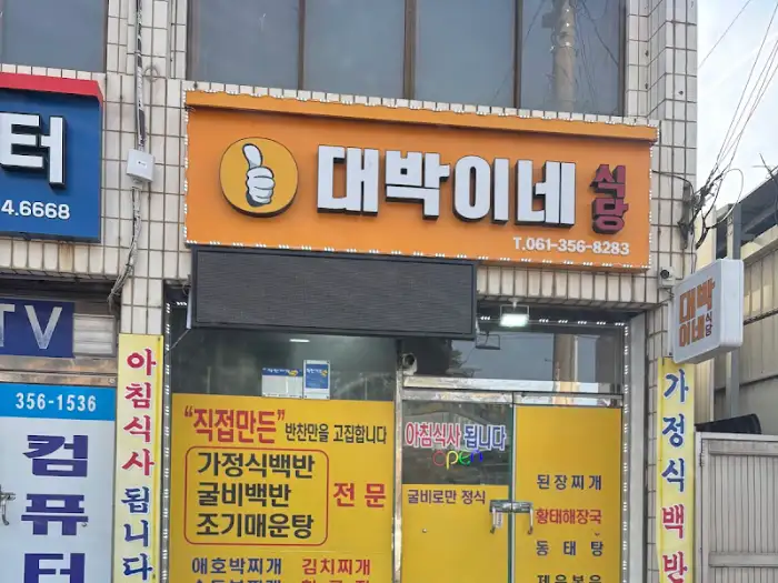 건물 외벽에 '대박이네 식당'이라는 큰 간판이 걸려 있습니다. 간판 옆에는 노란색 바탕에 검은 글씨로 쓰인 메뉴 안내문이 붙어 있습니다.