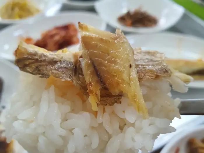 흰 쌀밥 위에 굴비 조각이 올려져 있습니다. 굴비는 노릇하게 잘 익었으며, 밥알은 윤기가 흐릅니다.
