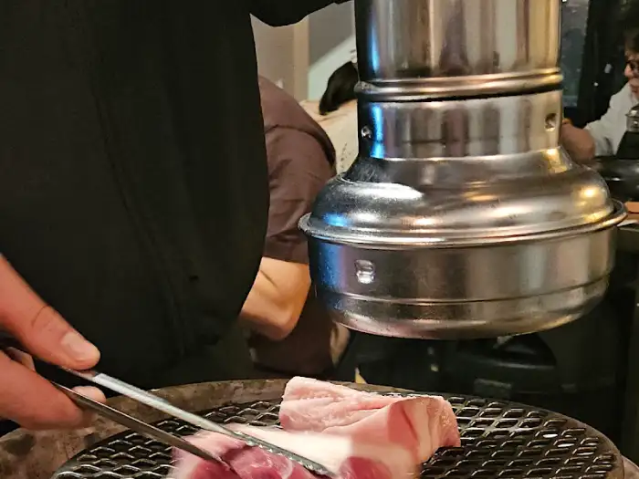뜨겁게 달궈진 불판 위에서 직원분이 집게로 고기를 뒤집고 있는 모습